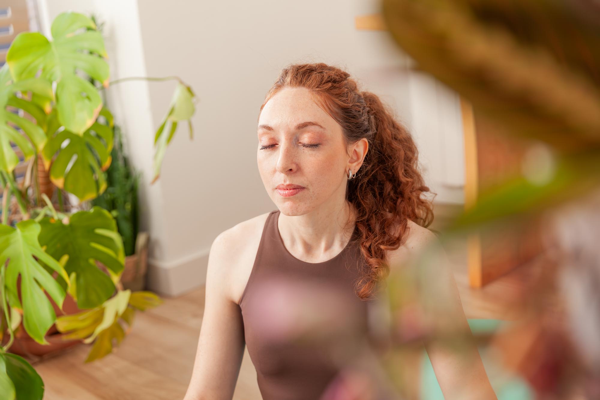 Person meditating indoors in a calm, plant-filled space