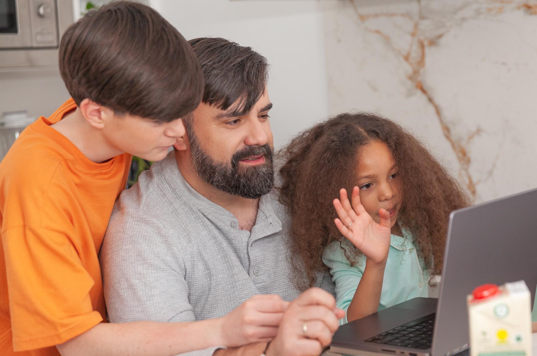 A father and kids sitting and looking at a laptop in a home setting