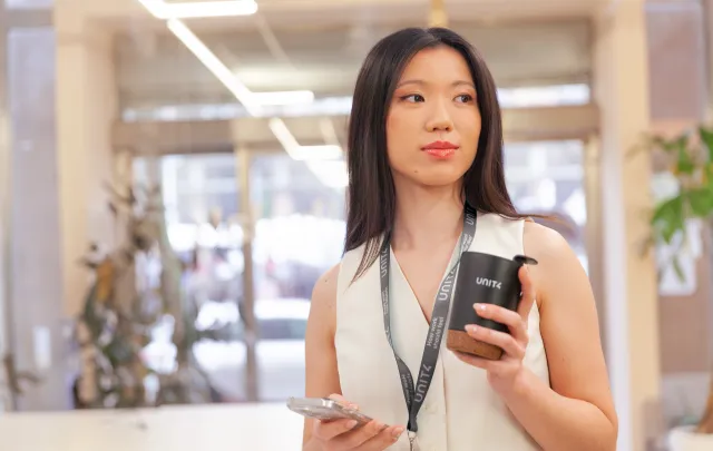 Person in a modern office enjoying a coffee while staying connected on their phone