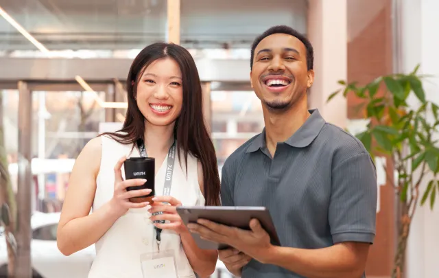 Two colleagues standing together, holding a phone and tablet in a modern office