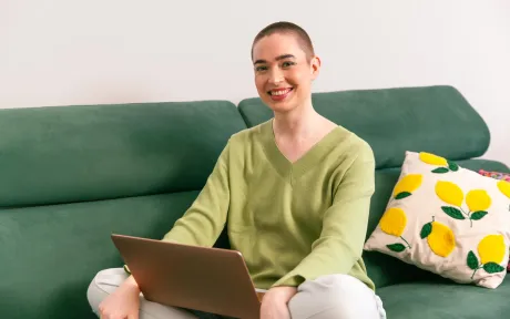 A person sitting on a sofa, working with a laptop at home