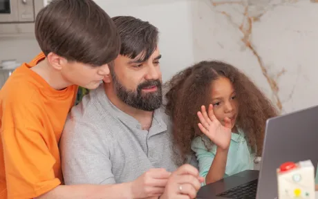 A father and kids sitting and looking at a laptop in a home setting