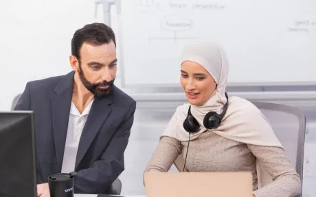 Colleagues sitting side by side, working together on computers in an office